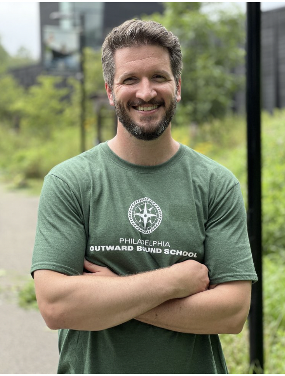 A man wearing an Outward Bound t-shirt smiling at the camera