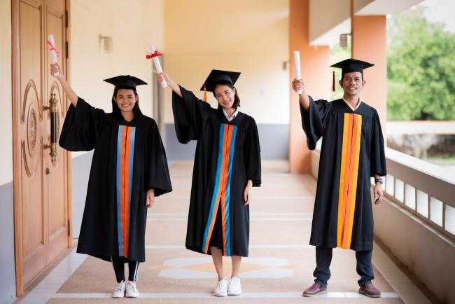 Three university graduates in caps and gowns, holding their diplomas aloft. 